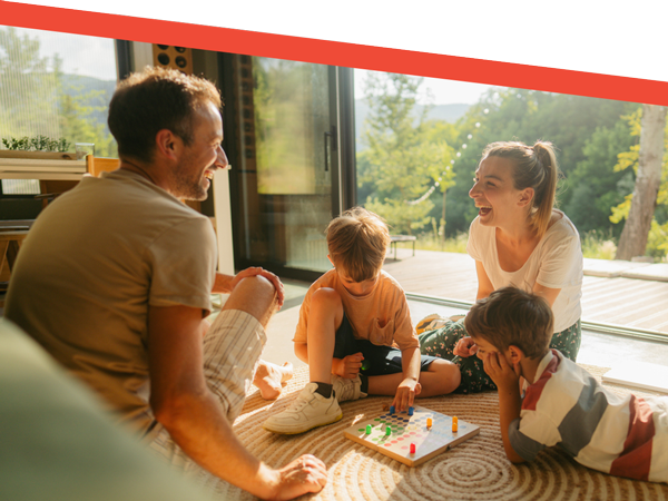 Smiling family of four enjoying a board game night in a sunlit living room by open glass doors